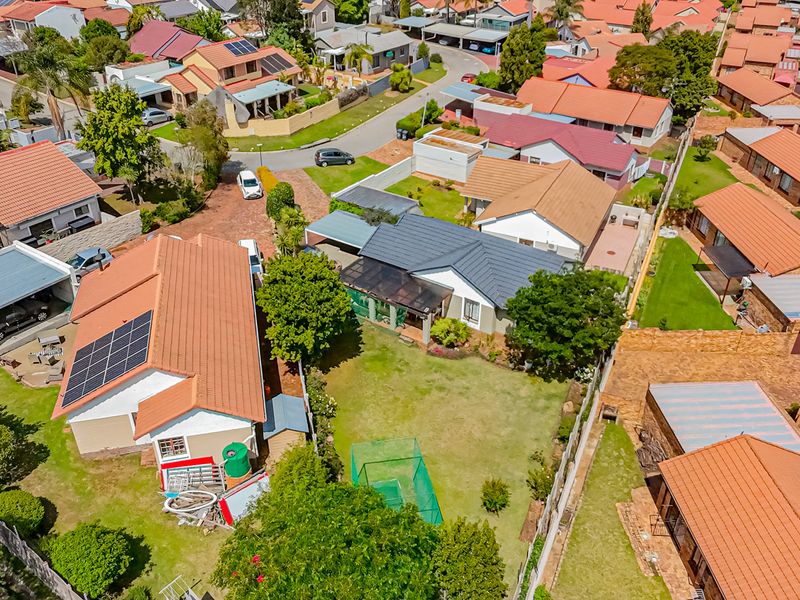 Aerial view of a residential property featuring a tiled roof, solar panels, a private garden, and a paved driveway within a suburban neighborhood.
