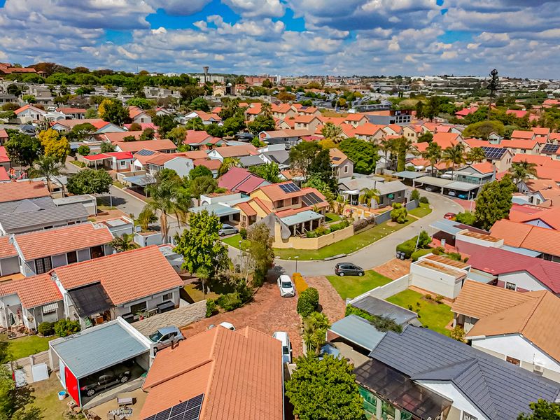 An aerial view of a residential estate featuring multiple houses with tiled roofs, solar installations, and paved street infrastructure.
