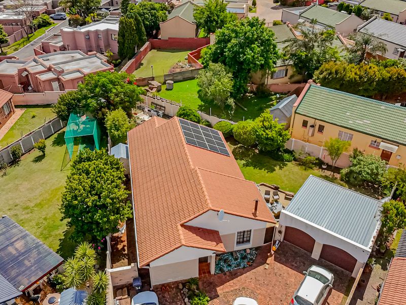 Aerial view of the property showcasing the tiled roof with solar panels, paved driveway, double garage, and surrounding garden area within a residential estate.