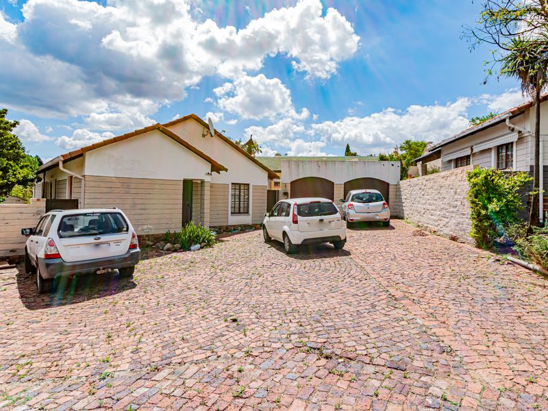 Front exterior view of the property featuring a cobblestone driveway, double garage, and stone boundary wall.