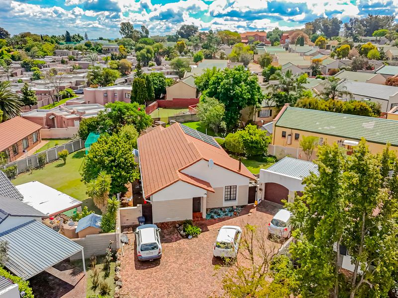 Aerial view of a residential property featuring a tiled roof, paved driveway, garage, and solar panels within a suburban estate setting.