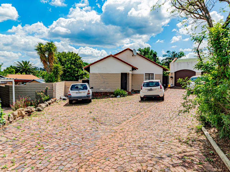 Front exterior view of the house featuring a large paved driveway, attached garage, and boundary walling.