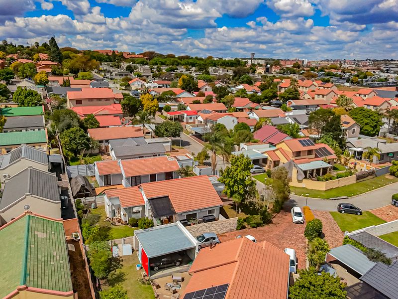 An aerial view of a residential housing estate featuring multiple homes with tiled roofs, paved driveways, and installed solar panels.