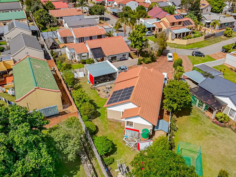 Aerial view of a residential property featuring a tiled roof with solar panels, a detached garage, and a private garden area within a suburban neighborhood.