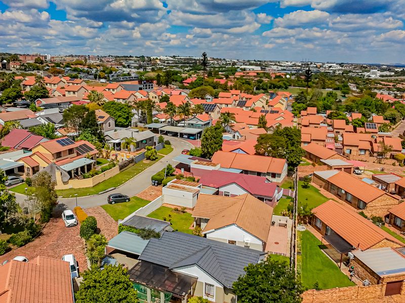 An aerial view of a residential housing estate featuring numerous homes with tiled roofs, paved driveways, and established gardens in a suburban setting.