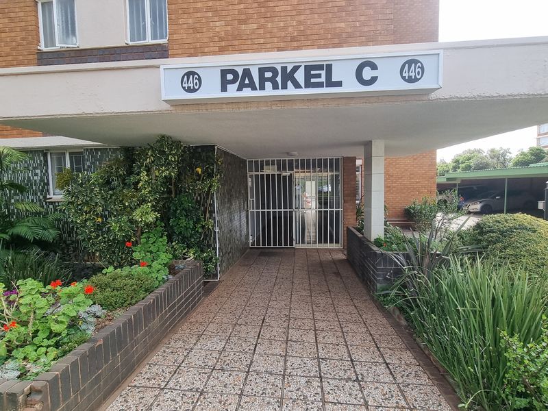 The front entrance of Parkel C features a covered canopy, secure gate access, and established brick planter boxes along a paved walkway.