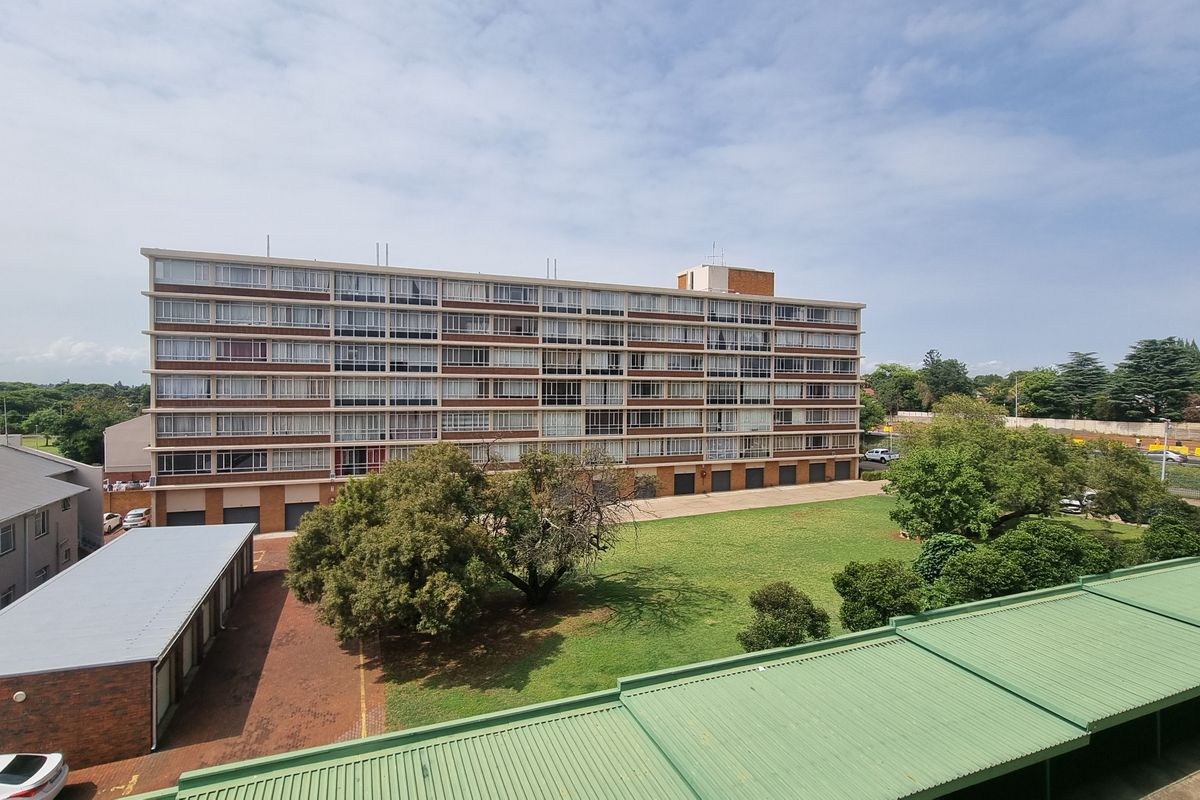 Elevated view of the apartment building exterior, featuring a brick facade, communal garden area, and covered parking facilities.