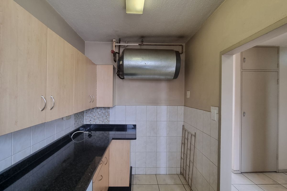 A compact kitchen featuring laminate cabinetry, granite countertops, and tiled splashbacks, with an exposed wall-mounted water heater.