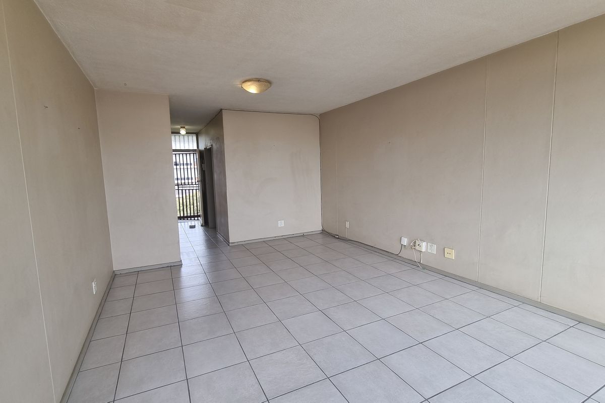 An empty, open-plan living area featuring neutral ceramic floor tiles and plain walls, providing a blank canvas for interior design and personalization.