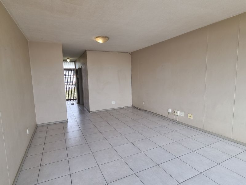 An empty, open-plan living area featuring neutral ceramic floor tiles and plain walls, providing a blank canvas for interior design and personalization.