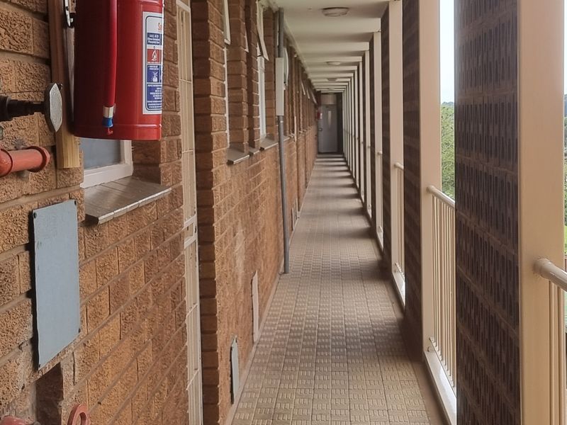 An exterior apartment building walkway featuring brick walls, tiled flooring, and metal safety railings overlooking the surrounding area.