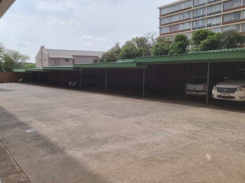 A row of covered parking bays featuring a metal roof structure and concrete paving, providing sheltered parking for residents.