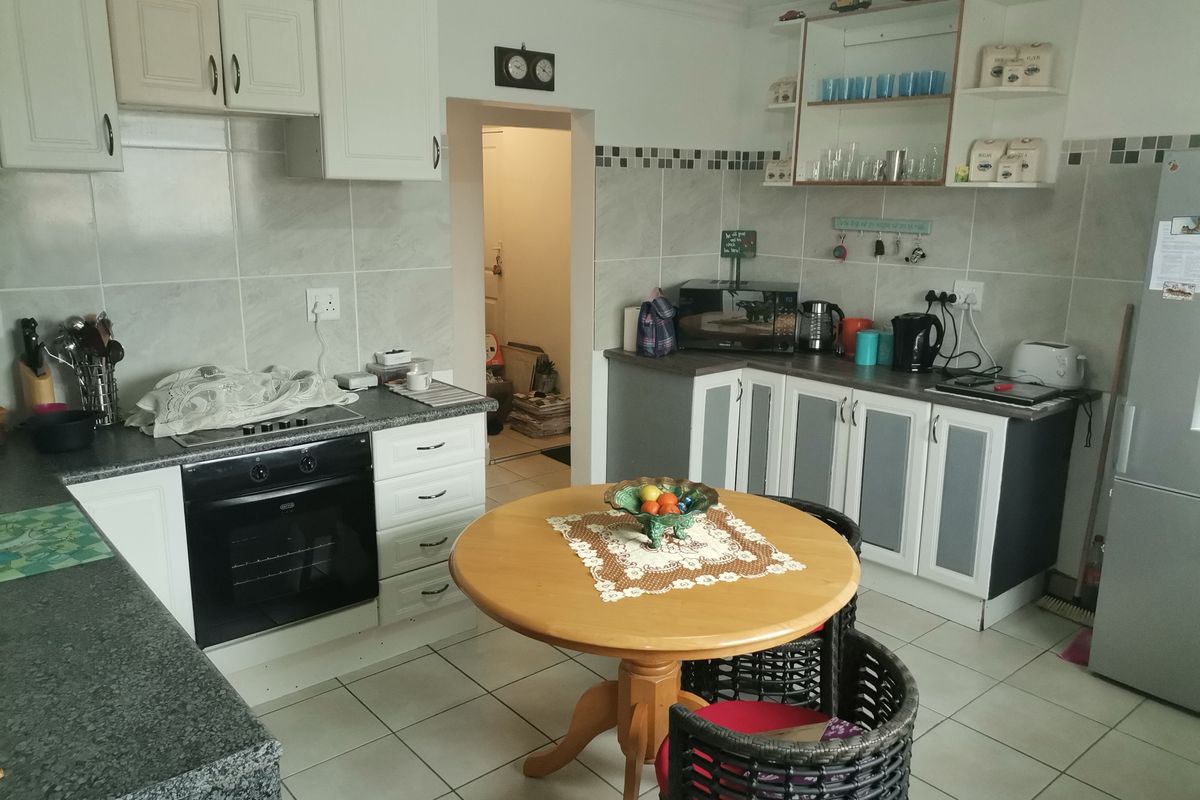 A functional kitchen featuring tiled flooring, laminate countertops, built-in oven, hob, and ample cabinetry with a tiled backsplash and open shelving.