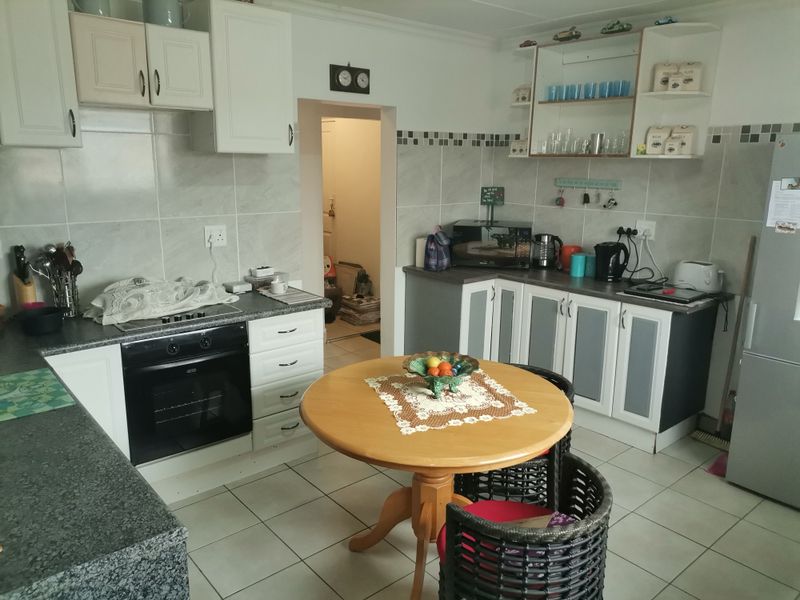 A functional kitchen featuring tiled flooring, laminate countertops, built-in oven, hob, and ample cabinetry with a tiled backsplash and open shelving.