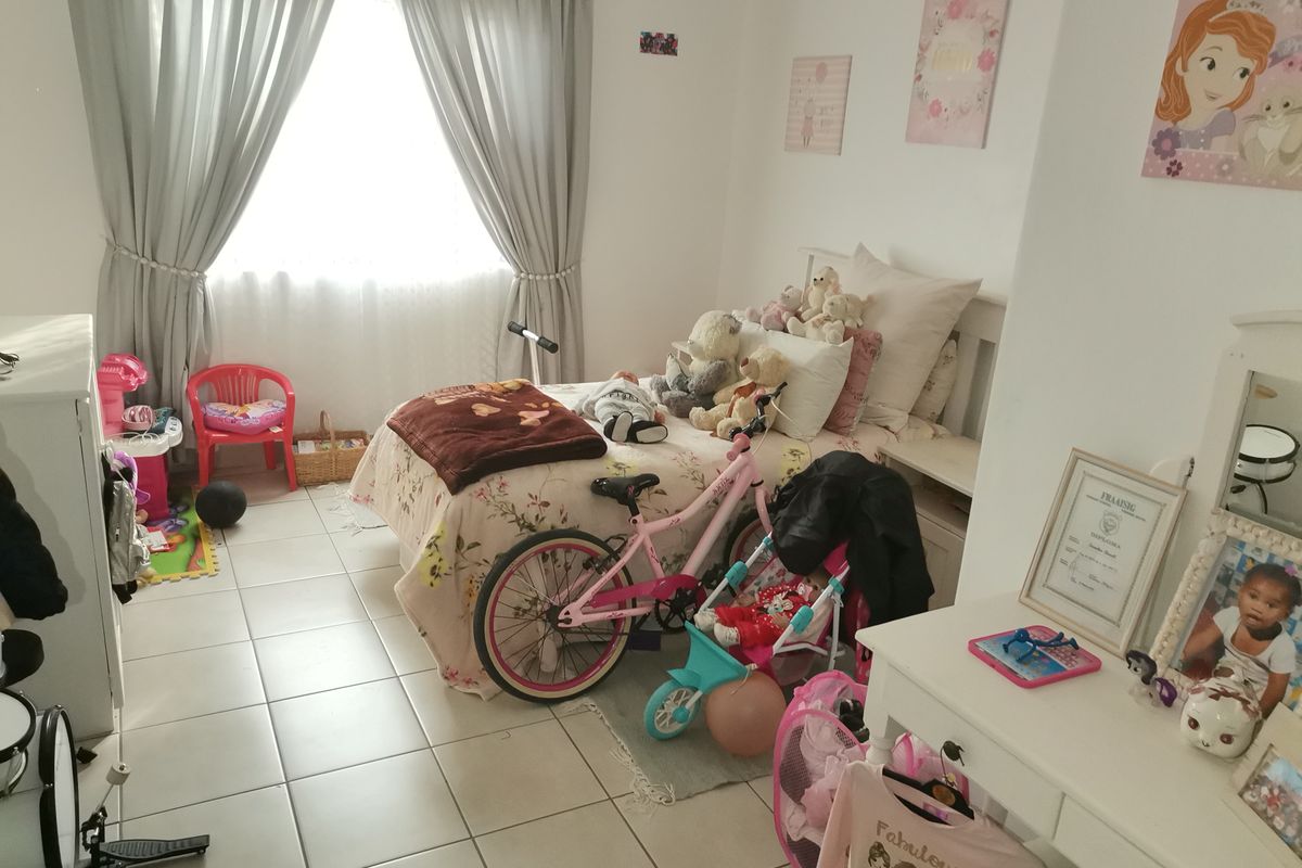 A bedroom featuring tiled flooring and window treatments, currently utilized as a child's room.