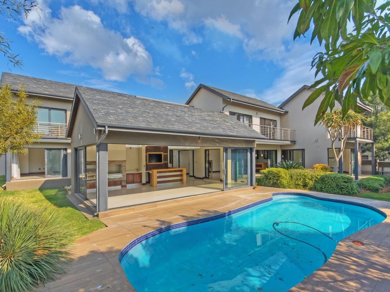 Rear view of the property featuring a swimming pool, tiled deck, and a spacious covered patio with built-in braai and sliding glass doors.