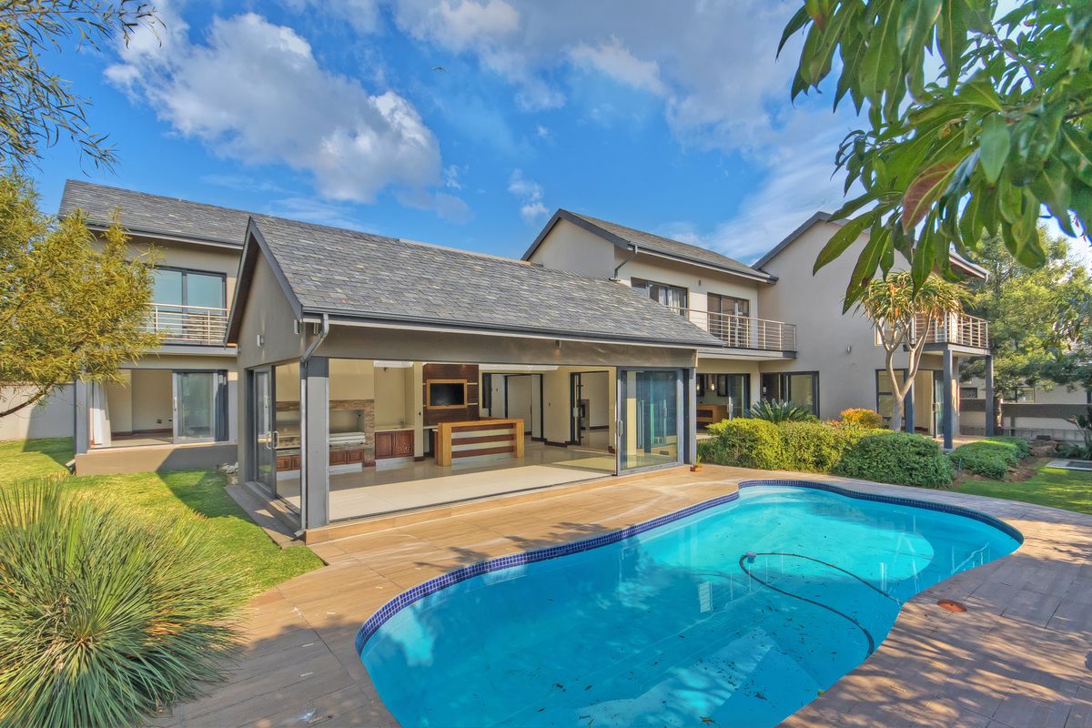 Rear view of the property featuring a swimming pool, tiled deck, and a spacious covered patio with built-in braai and sliding glass doors.