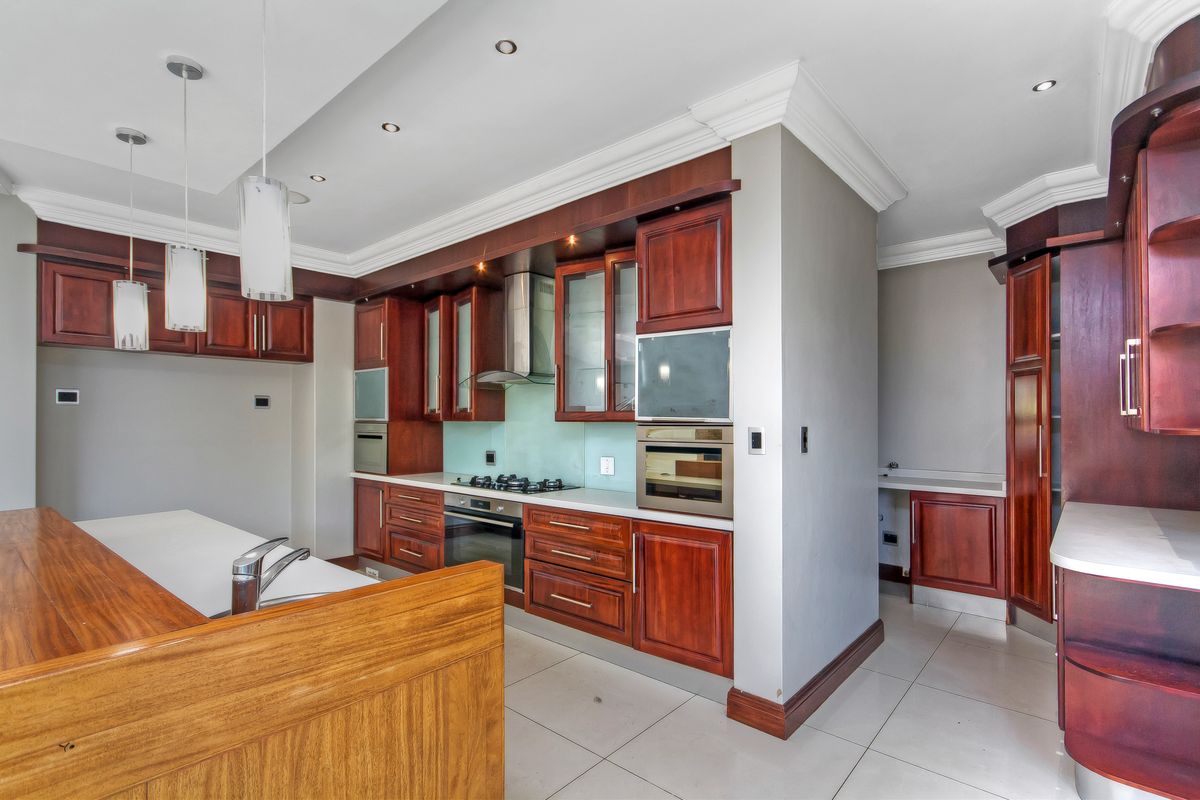 A spacious, modern kitchen featuring rich wood cabinetry, stone countertops, integrated appliances, and a functional layout with a breakfast bar and tiled flooring.