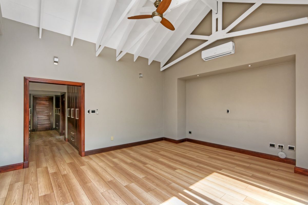 Spacious bedroom featuring vaulted ceilings with exposed rafters, laminate flooring, built-in cupboards, and a split-system air conditioner.