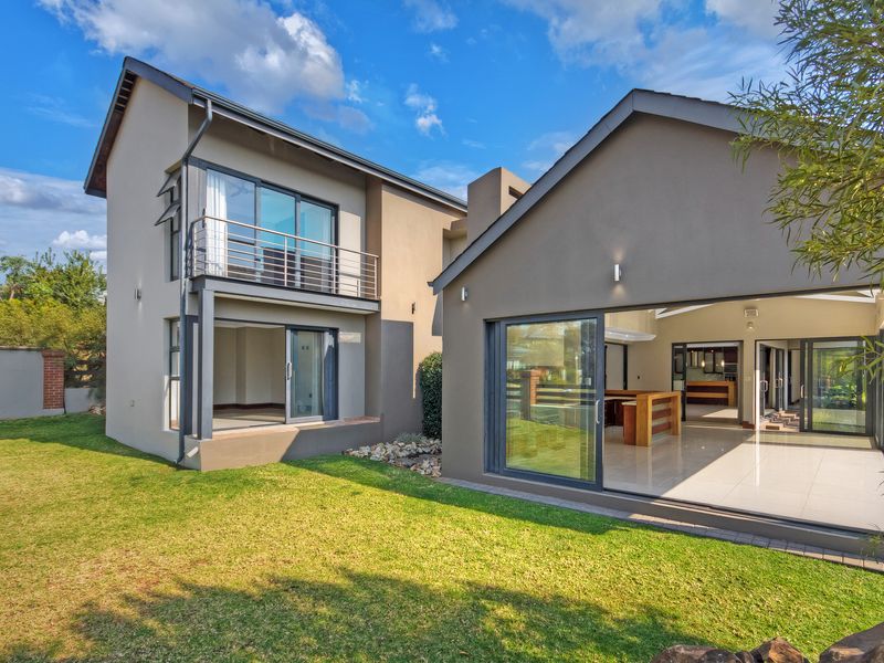 Rear view of a modern two-story house featuring large sliding glass doors, a balcony, and a well-maintained garden.