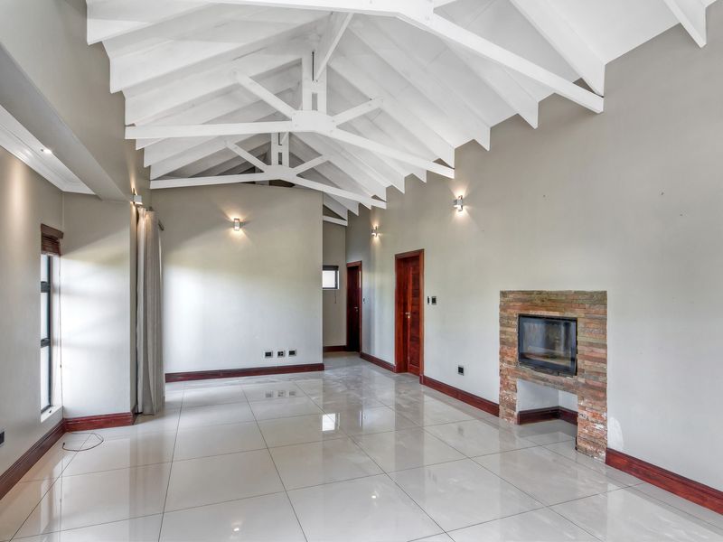 Spacious living area featuring a high vaulted ceiling with exposed white trusses, polished tiled floors, and a built-in brick fireplace.