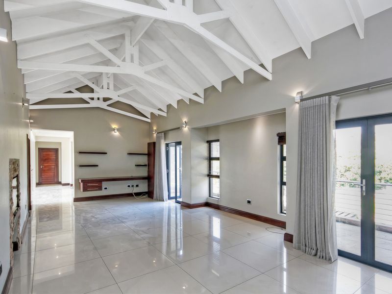 Spacious living area featuring a high vaulted ceiling with exposed trusses, polished porcelain tiles, a built-in desk, and direct access to an outdoor patio.