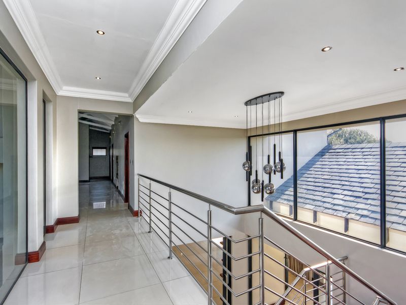 A bright, modern upper-level hallway featuring polished porcelain tiles, a sleek stainless steel balustrade, and a contemporary multi-pendant light fixture.