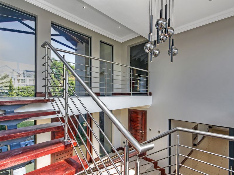 Spacious double-volume entrance hall featuring a timber staircase with stainless steel balustrades, modern pendant lighting, and large windows providing ample natural light.