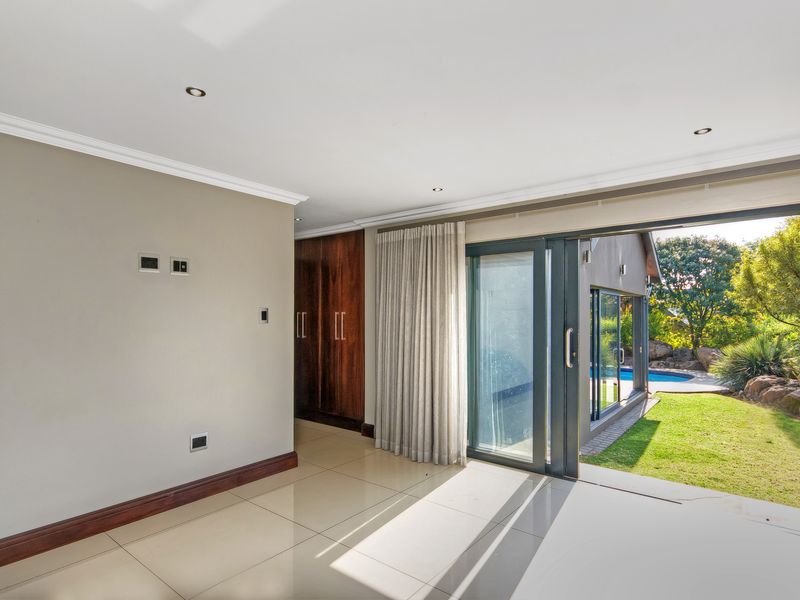 Spacious living area featuring large sliding glass doors opening to a garden and pool, with tiled floors and built-in storage cabinetry.