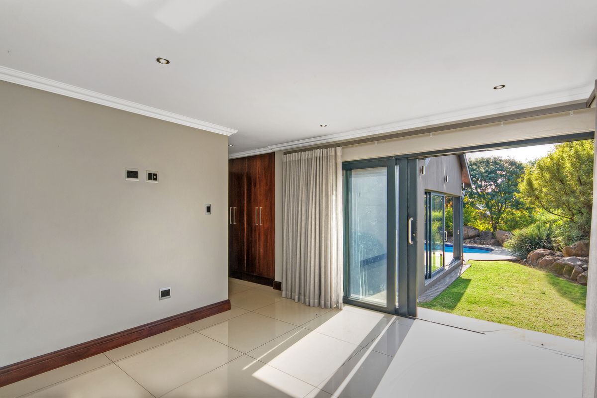 Spacious living area featuring large sliding glass doors opening to a garden and pool, with tiled floors and built-in storage cabinetry.