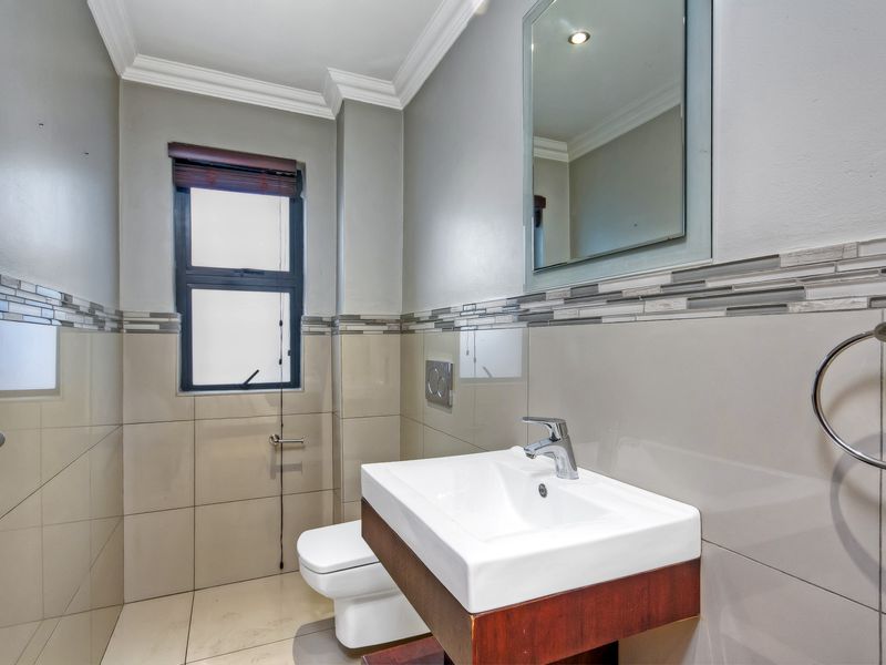 A modern bathroom featuring a wall-mounted vanity with a ceramic basin, wall-hung toilet, and neutral tiled walls with a decorative mosaic border.