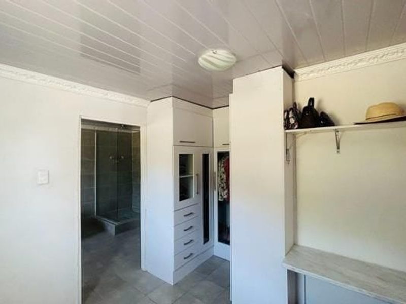 Bedroom featuring built-in cupboards and an en-suite bathroom with a glass shower enclosure, finished with tiled flooring and ceiling cladding.
