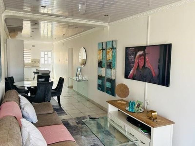 Open-plan living and dining area featuring tiled flooring and a glossy ceiling finish, creating a connected space leading toward the kitchen.