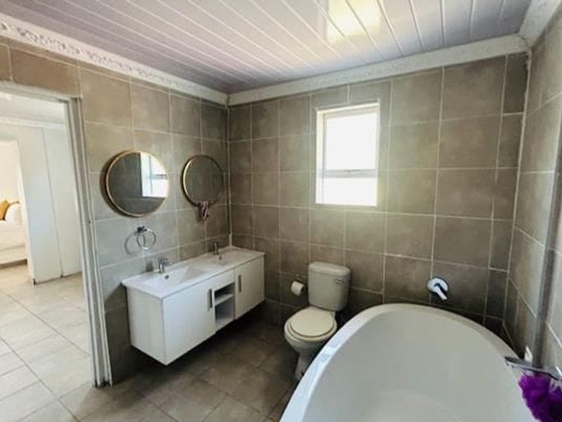 A well-maintained bathroom featuring a double vanity, a modern freestanding bathtub, and neutral floor-to-ceiling tiling.