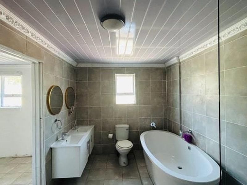A well-maintained bathroom featuring a freestanding bathtub, dual vanity unit, and neutral wall tiling with a modern PVC ceiling finish.