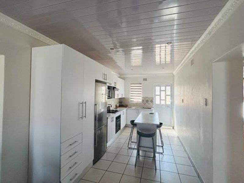 A clean, modern kitchen featuring white cabinetry, a central island, tiled flooring, and a glossy PVC ceiling with integrated lighting.