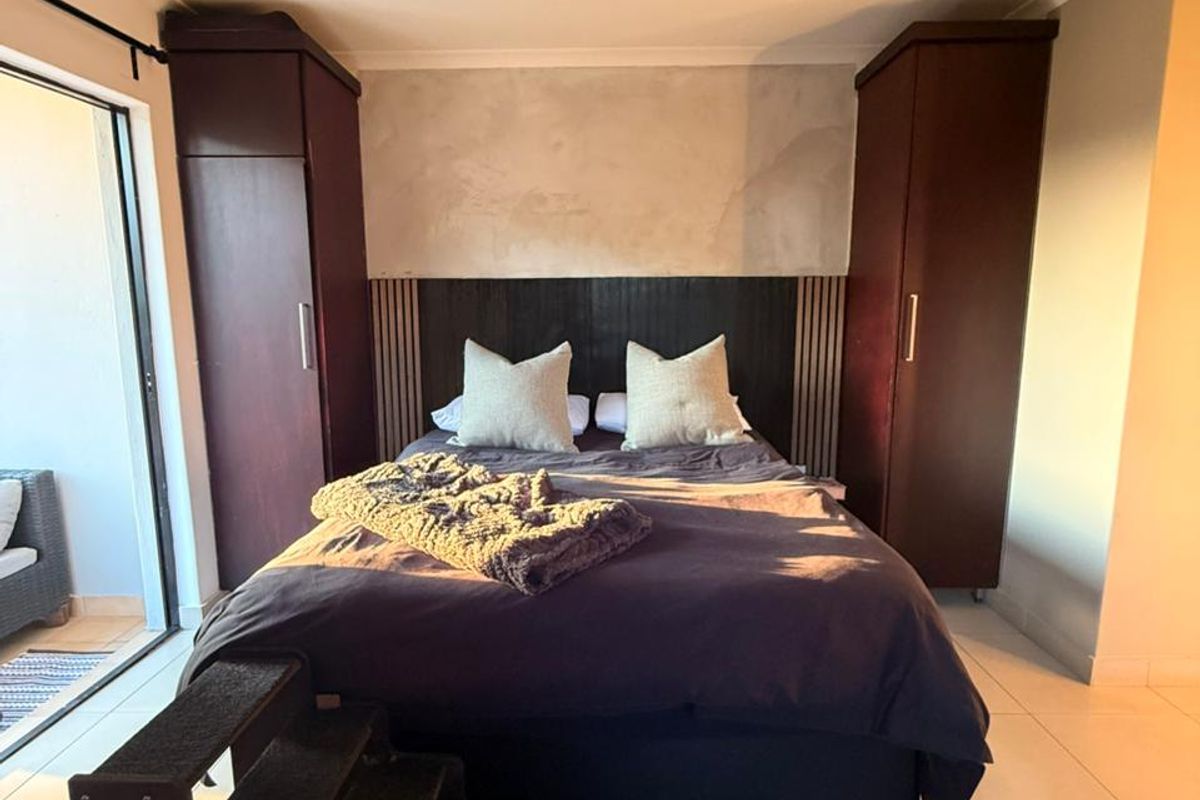 A well-lit bedroom featuring built-in dark wood wardrobes, a decorative headboard wall, and sliding door access to an outdoor patio area.