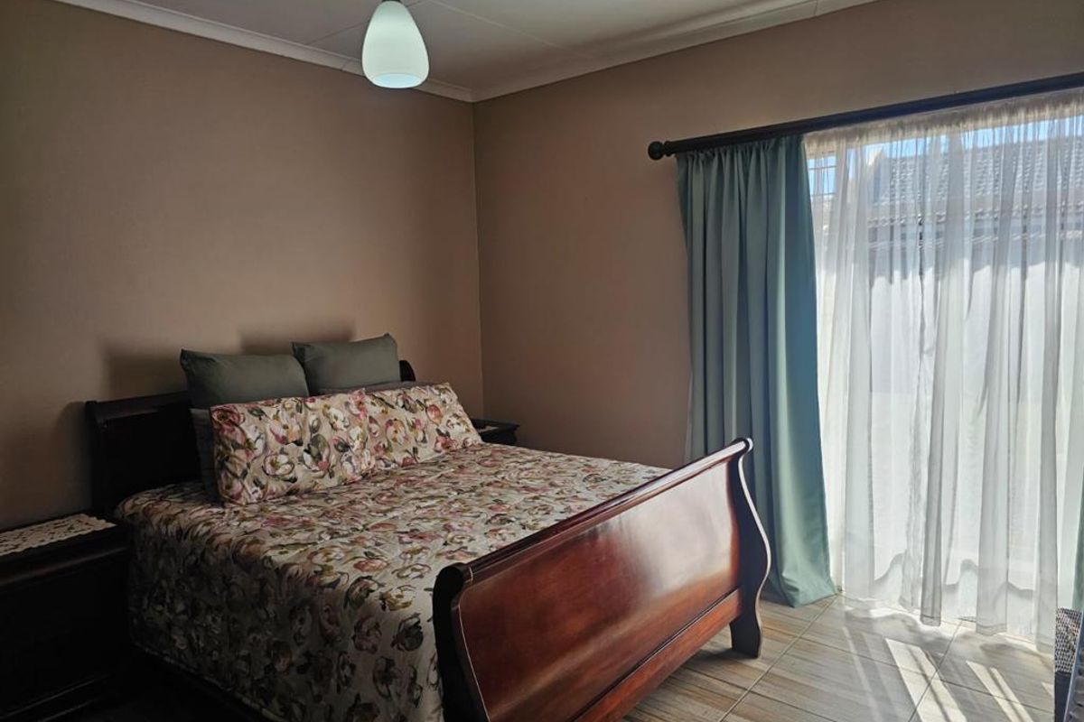 A bedroom featuring tiled flooring, neutral wall tones, and a large window with curtain treatments, providing natural light.