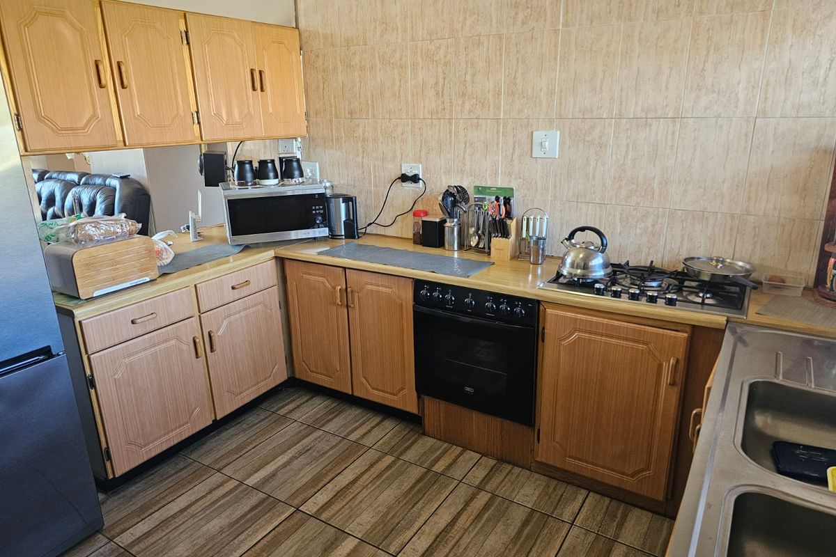 A functional kitchen featuring wood-look cabinetry, tiled splashbacks, a built-in oven with gas hob, and tiled flooring.