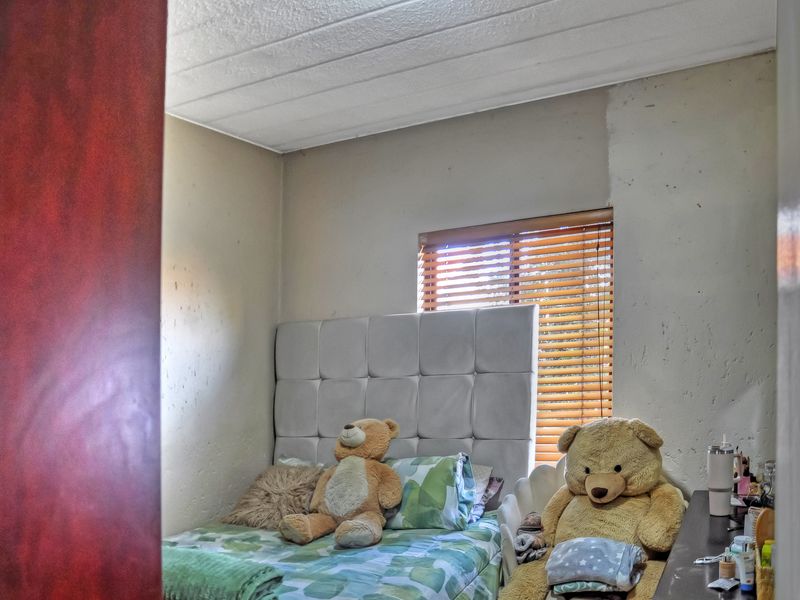 A bedroom featuring a textured ceiling and venetian blinds, currently showing signs of wear including unfinished wall paint and surface staining.