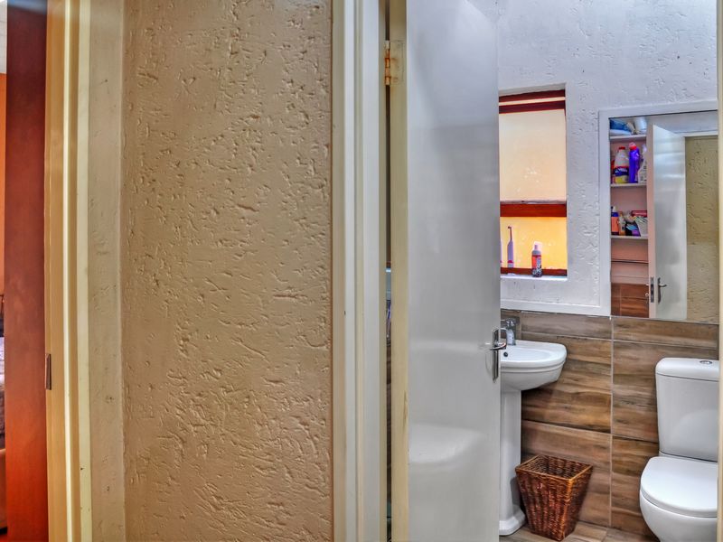 A compact bathroom featuring a pedestal basin, toilet, and tiled wall finishes, with a view into an adjacent bedroom.