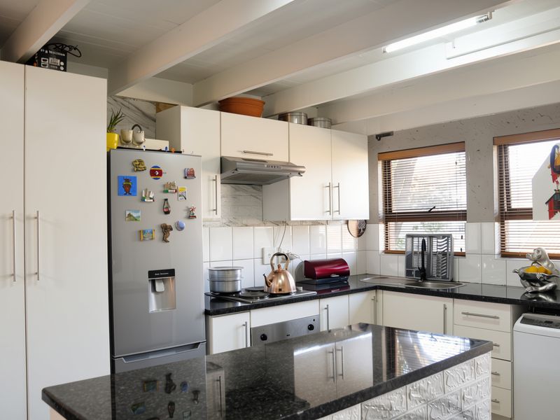 A functional kitchen featuring white cabinetry, black granite countertops, a tiled backsplash, and exposed ceiling beams with a skylight for natural light.