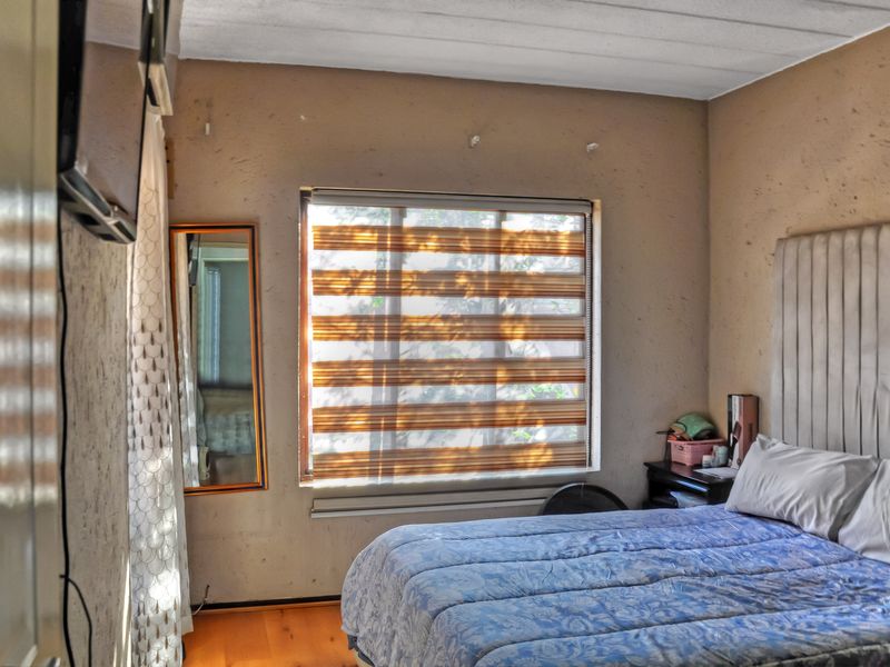 A bedroom featuring textured walls, laminate flooring, and modern zebra blinds, offering a functional space with potential for cosmetic updates.
