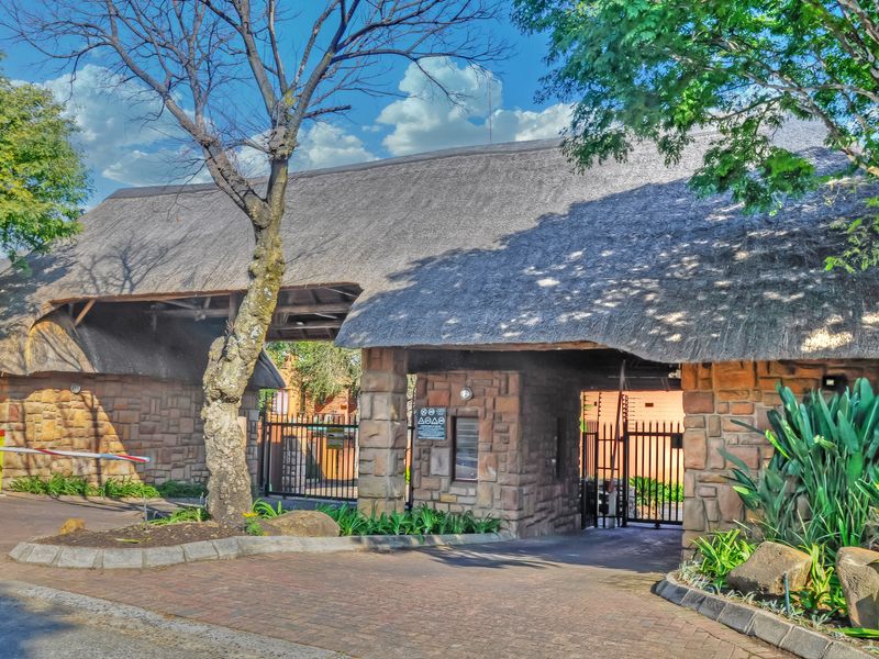 The property features a secure entrance with a distinctive thatched roof, stone-clad pillars, a boom gate, and a paved driveway.
