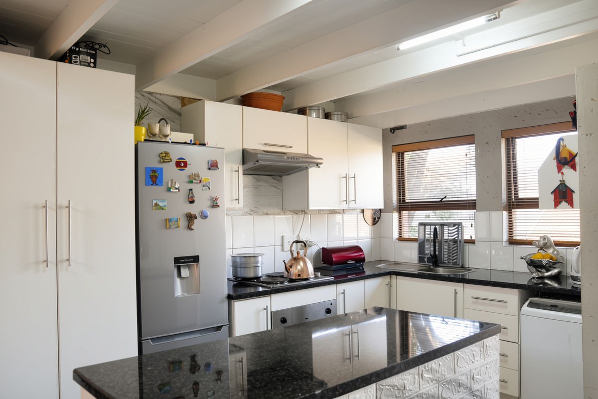 A functional kitchen featuring white cabinetry, black granite countertops, a tiled backsplash, and exposed ceiling beams with a skylight for natural light.