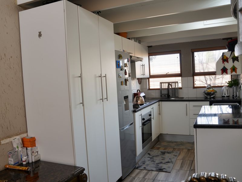 A functional kitchen featuring white cabinetry, built-in oven and hob, dark countertops, and exposed ceiling beams with natural light from two windows.