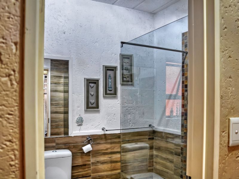 A modern bathroom featuring a glass shower screen, wood-look wall tiling, and a textured wall finish.