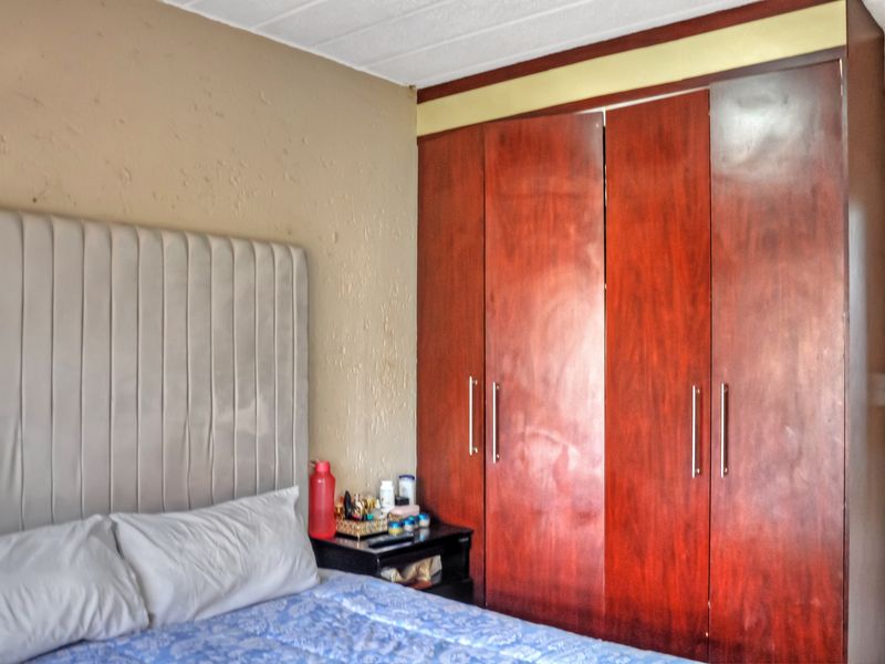 A bedroom featuring a large built-in wooden wardrobe and textured wall finishes, offering potential for cosmetic updates to modernize the space.