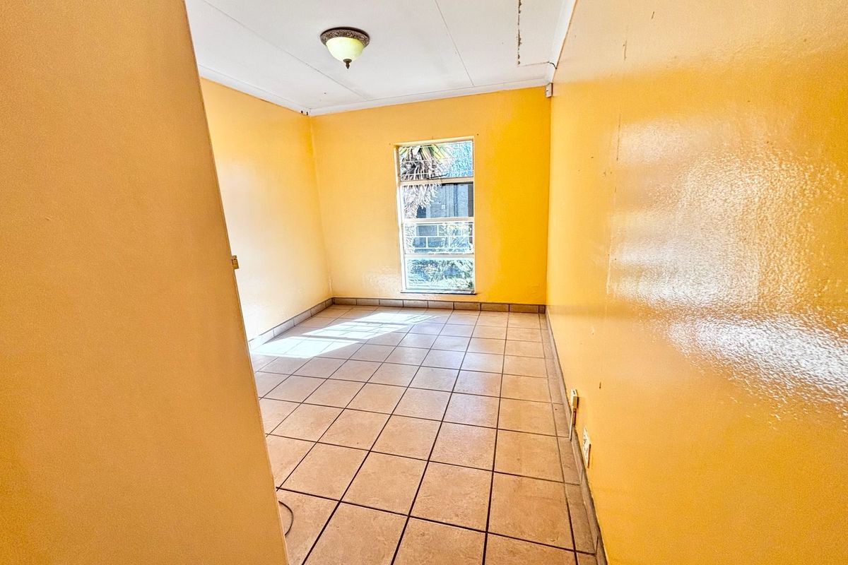 An empty bedroom featuring tiled flooring and yellow walls, requiring cosmetic updates and ceiling repairs.