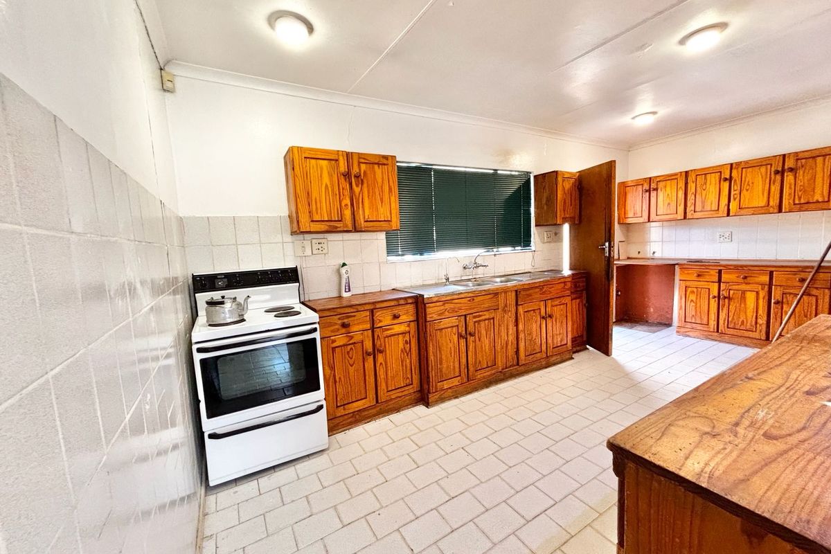 A spacious kitchen featuring wooden cabinetry, tiled flooring, and a tiled splashback, offering a functional layout ready for modernization.